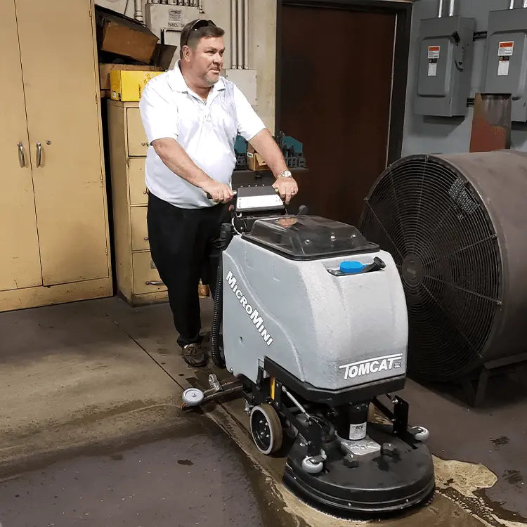 Walk-behind floor scrubber in workshop with gray body and black base