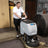 Walk-behind floor scrubber in workshop with gray body and black base